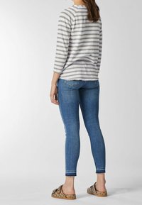 Gray and white striped long-sleeve top, blue fitted jeans, and brown slide shoes with a bow accent, viewed from the back.