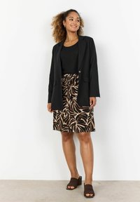 Schwarzes Blazer über einem schwarzen Oberteil, kombiniert mit einem braunen gemusterten Rock mit Blättermotiven und braunen Keilsandalen. Glatte Texturen durchgehend.
