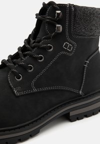 Bota de ante negra con un cuello texturizado gris, ojales metálicos, cordones negros y costuras blancas en contraste sobre una suela resistente.