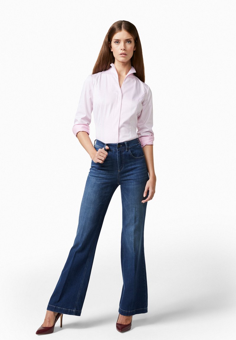 Camicia fitted rosa chiaro con maniche lunghe, abbinata a jeans a palazzo blu scuro e tacchi alti color bordeaux, su sfondo bianco.