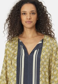 Camicia col colletto a V. Un lato in verde oliva con motivi floreali, l'altro in blu navy con strisce verticali. Tessuto leggero.