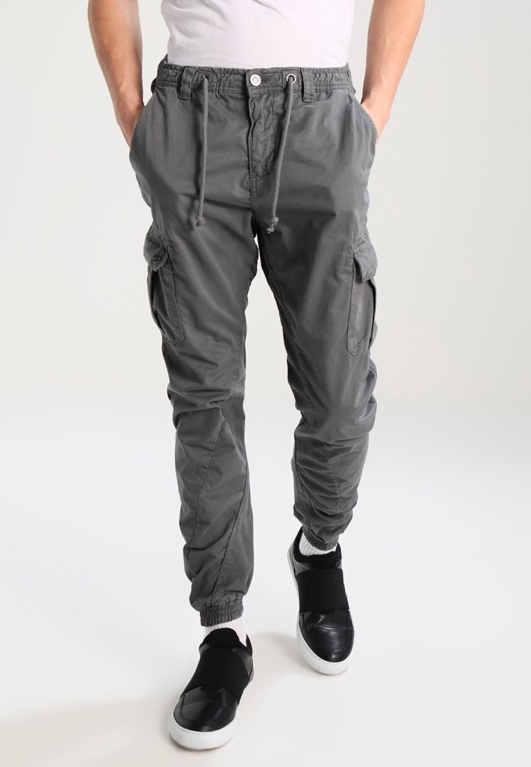 Homme portant un pantalon jogger cargo gris avec des poignets élastiques et une taille à cordon, assorti à des baskets noires sans lacets et des chaussettes blanches.