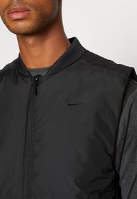 Schwarze Nike Bomberjacke mit Reißverschluss vorne, glatter Textur und geripptem Kragen. Verfügt über ein dezentes Logo auf der Brust und hat ein leichtes Design.