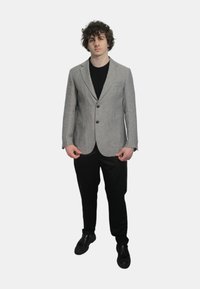Blazer a righe grigie e bianche con revers e due bottoni, indossato su una camicia nera, abbinato a pantaloni neri e scarpe.
