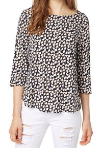 Maglietta a maniche lunghe con un motivo astratto navy e crema, scollatura rotonda, tessuto morbido e vestibilità comoda. Abbinata a jeans bianchi strappati.