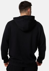 Sudadera negra de material suave, con bolsillo tipo canguro y capucha ajustable con cordón. Puños y dobladillo acanalados para un ajuste ceñido.
