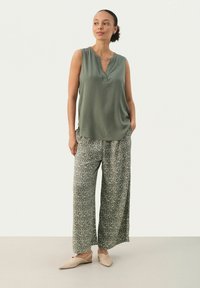Top fără mâneci de culoare verde măslin, cu decolteu în V, asortat cu pantaloni largi gri cu un model, lejeri, și pantofi plate de culoare bej deschis. Textură de material neted.