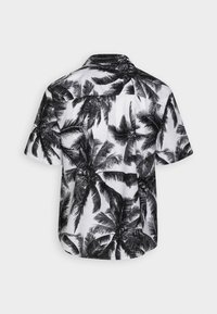Chemise à manches courtes en tissu blanc avec imprimé de palmiers noirs. Le modèle comprend un col classique et une coupe droite.