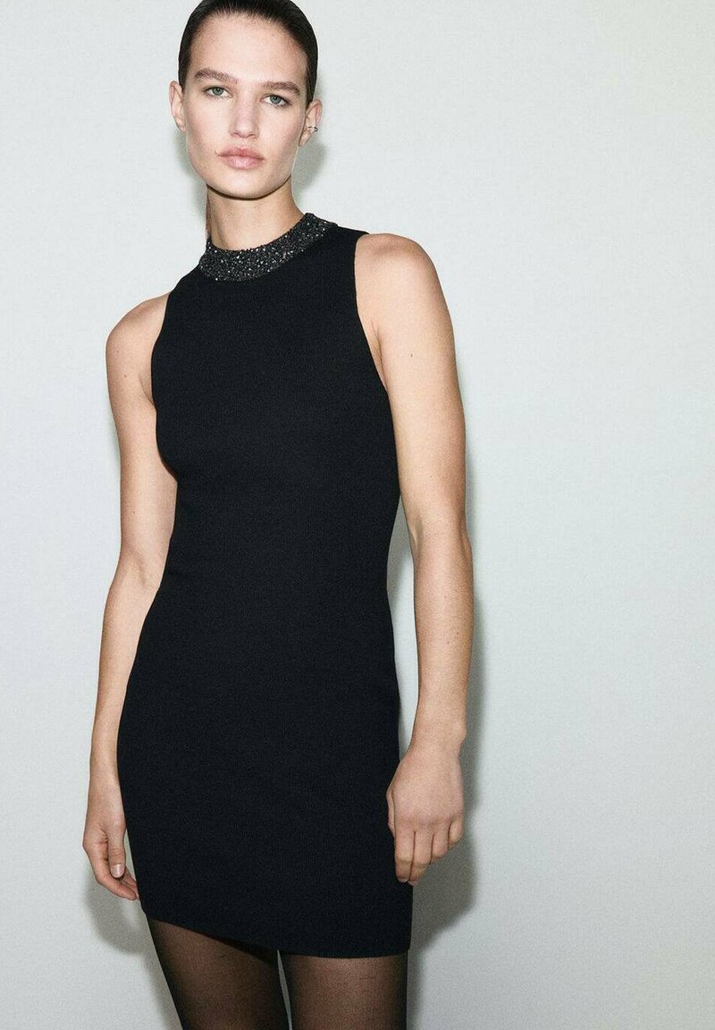 Vestido de punto sin mangas de color negro con un cuello texturizado y embellecido. Silueta ceñida, tela suave y longitud por encima de la rodilla.