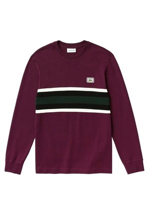 Chemise à manches longues bordeaux avec des rayures horizontales blanches et vert foncé sur la poitrine, ornée d'un petit écusson logo crocodile Lacoste.