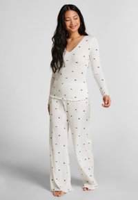 Conjunto de loungewear blanco que presenta mangas largas, textura acanalada y patrones florales. Los pantalones tienen un corte holgado con dobladillos ondulados y sutiles embellishments.