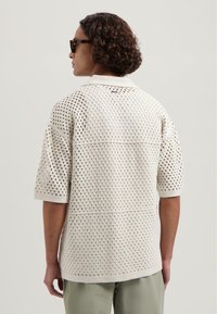 Romiggekleurige, open-gehaakte shirt met een relaxte pasvorm, korte mouwen en een gestructureerd patroon. Heeft een klassieke kraag en een rechte zoom.