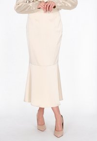 Falda lápiz de satén color crema con dobladillo acampanado, que presenta una textura suave y un diseño sin costuras. Combinada con tacones nude de punta afilada.