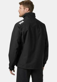 Chaqueta impermeable negra con cuello alto, diseño de ventilación en la parte posterior y gran logo blanco en el hombro. Tejido texturizado y ajuste relajado.