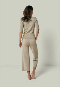 Beige gestricktes Oberteil mit kurzen Ärmeln und passenden weiten Hosen, mit einem strukturierten Muster, von hinten auf einem hellgrünen Hintergrund gezeigt.