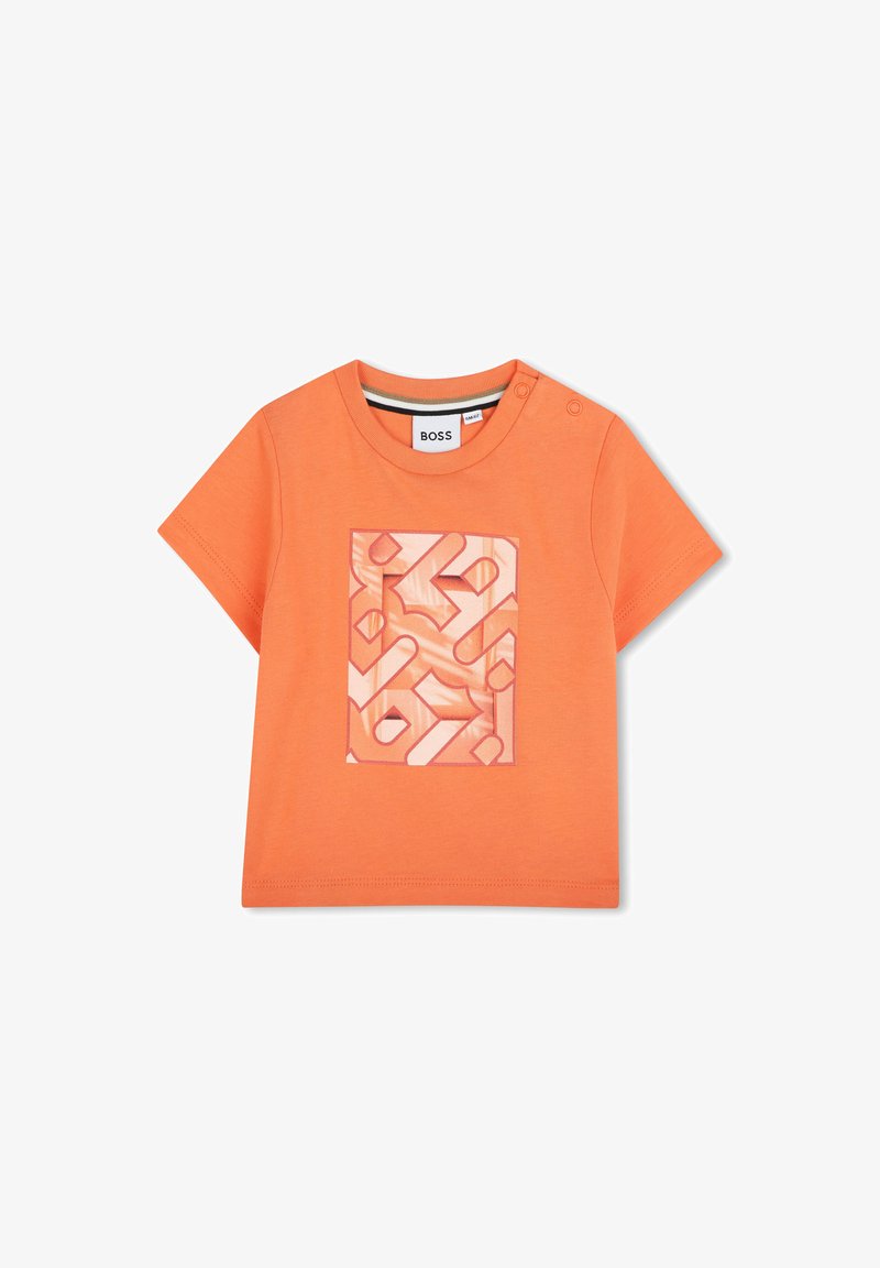 Oranje katoenen T-shirt met een rechthoekig gedrukt ontwerp met abstracte vormen in tinten roze en koraal. Twee drukknoopjes op de schouders voor gemakkelijk aan- en uittrekken.