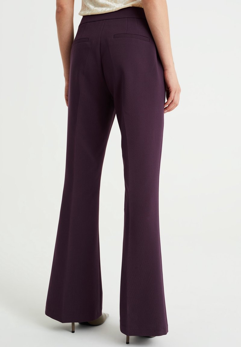 Pantaloni a zampa d'elefante in tessuto di un profondo viola, con una superficie liscia e tasche posteriori. La cintura è piatta e sagomata per una vestibilità strutturata.