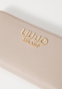 Portafoglio in pelle beige chiaro con superficie testurizzata e logo dorato in rilievo "LIU·JO MILANO" sul fronte.