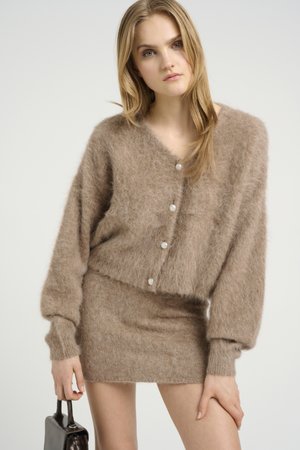 Bruine mohair cardigan met een cropped ontwerp, voorzien van grote knopen en lange mouwen, gecombineerd met een bijpassende aansluitende rok. Eenvoudige handtas.