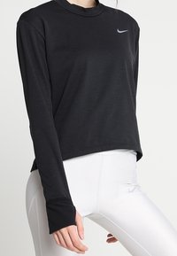 T-shirt de sport noir à manches longues en tissu léger avec un col rond et un logo Nike gris discret sur le haut à gauche.