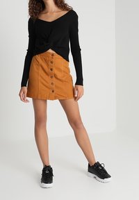 Svart långärmad topp med knutdetalj, kombinerad med en orange denimkjol med framknappar och svarta sneakers med vita sulor.