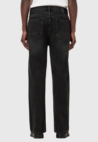 Schwarze Jeans aus Denim mit geradem Bein, sichtbaren Nähten und zwei Gesäßtaschen. Das Material hat ein modernes, strukturiertes Finish.