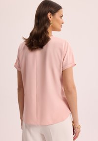 Różowa bluzka z krótkim rękawem o miękkiej, gładkiej teksturze. Posiada zaokrąglony dół i detal szwu na plecach. Odpowiednia na różne okazje.