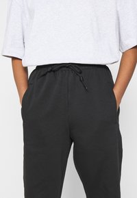 Svarta joggerbyxor med dragsko och sidofickor, tillverkade av mjukt tyg; matchas med en ljusgrå t-shirt med kort ärm.