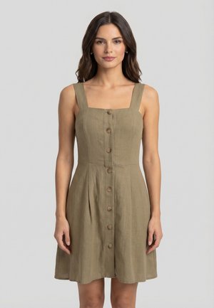 Femme portant une robe sans manches vert olive à boutons sur le devant avec un décolleté carré, debout devant un fond clair uni.