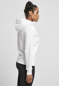 Hvit hettegenser med snor, lange ermer og ribbede mansjetter. Kombinert med svarte leggings, og viser et enkelt og avslappet design.