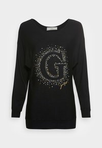 Schwarzes Langarmoberteil mit einem großen metallischen "G"-Design, umgeben von Punkten in Silber, Gold und Weiß. Weicher Stoff mit gerippten Bündchen.