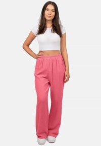 Rosa strukturierte weite Hose mit elastischem Bund, kombiniert mit einem weißen, enganliegenden Crop-Top und weißen Schuhen. Einfaches und lässiges Design.