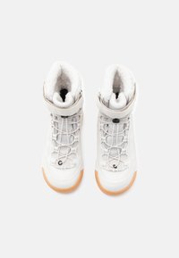 Zapatos altos blancos de material texturizado, con acolchado en el cuello y suela de goma. Presenta una correa y un intrincado sistema de cordones. Forro interior suave.