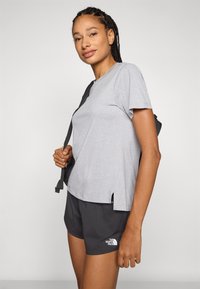 Grijze t-shirt met korte mouwen, in een comfortabele pasvorm en met zijsplitten, gecombineerd met zwarte shorts met een subtiel ruitpatroon en een wit logo.