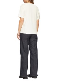 Witte korte mouwen t-shirt gezien vanuit de achterkant, gecombineerd met donkerblauwe wijde denim jeans. De stof lijkt soepel en casual.