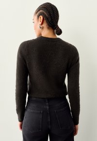 Donkere, pluizige trui met ronde halslijn, afgebeeld tegen een lichte achtergrond; gecombineerd met hooggetailleerde zwarte jeans met achterzakken.