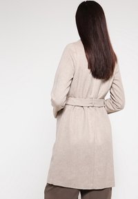 Cappotto in misto lana beige con vita avvitata, design di lunghezza media e texture liscia. Presenta una silhouette pulita e dettagli minimi.