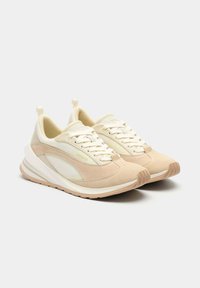 Zapatillas beige que combinan tela lisa y ante. Diseño con cordones, acolchado, suelas texturizadas y tiradores en el talón.