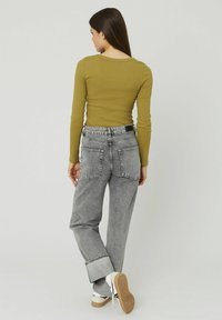 Un haut à manches longues vert olive associé à un jean baggy gris délavé taille haute et des baskets blanches avec des accents noirs et blancs.
