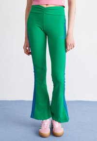 Gröna ribbade utställda byxor med blå sidostriper. Har en rynkad midja och en liten blå logotyp vid höften. Sammanfogas med rosa sneakers.