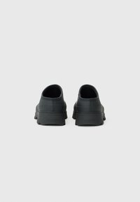 Black rubber shoes with a low-profile design, smooth texture, and minimal detailing, featuring a textured sole and heel branding.