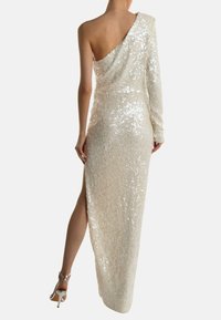 Yhden olkapään, lattiaan ulottuva mekko ivorin värissä, joka on kokonaan päällystetty paljeteilla. Siinä on sivureikä ja tiukka siluetti, jota korostavat pitkät hihat.