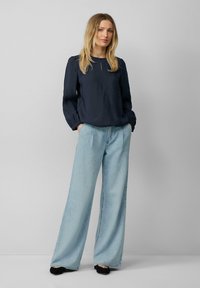 Blouse bleu marine à col rond et manches bouffantes, assortie à un jean bleu clair à jambes larges. Des chaussures noires complètent l'ensemble.