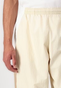 Calças de cor clara e textura, com um cós elástico e bolsos laterais, apresentando um corte solto e um tecido macio e leve.
