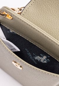 Lys olivengrøn struktureret lædertaske indvendigt med et guld accenter og sort foring med et logo. Indeholder labels inde i lommen.