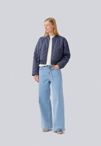 Navy quilted cropped jacket with a round neckline, paired with light blue wide-leg jeans and minimal strappy sandals. Smooth fabric texture.