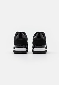 Baskets noires combinant mesh et suède, avec des accents noirs brillants, des semelles rembourrées, et une semelle extérieure blanche et noire.