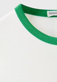 Encolure de t-shirt blanche avec col côtelé vert et une étiquette visible à l'intérieur au dos montrant une partie du nom de la marque.