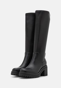 Bottes noires montantes en cuir poli avec une semelle texturée, un talon bloc et un design supérieur lisse. Présente un détail de couture minimaliste.