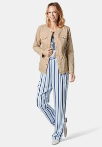 Lichtbeige jas met gouden hardware, gecombineerd met blauw-witte gestreepte wijde broek. De top heeft bloemenpatronen in blauw en groen.